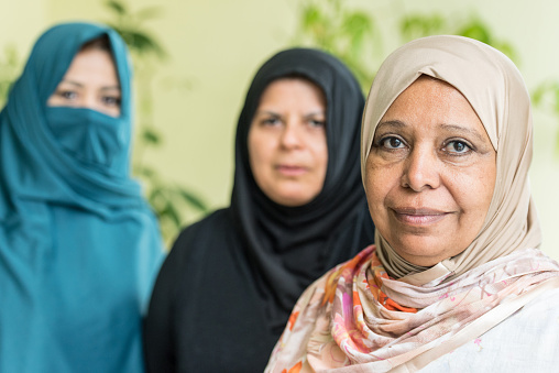 close up picture of a smiling mature middle eastern muslim woman wearing a veil with two other muslim women in the background