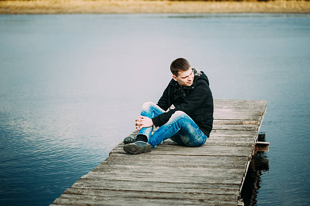 istock Young handsome man sitting on wooden pier, relaxing,  thinking, 531318203