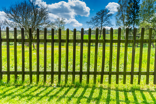 Landscape with old wooden railing with cloudy dramatic sky and trees. Grass field with fence cloudy sky and beautiful nature.