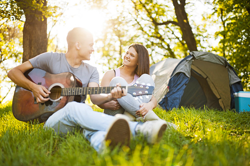 Teenage couple on camping. Boyfriend is playing the guitar to his girlfriend.  