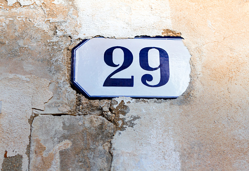 A cracked vintage white and blue ceramic number 29 address tile on a mottled crumbling old orangish-whitish wall. Shot in Italy. Copy space available.
