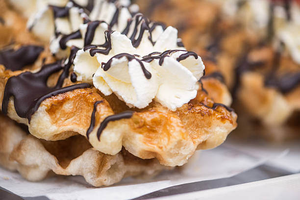 Close up of traditional large Belgian waffles with whipped cream and dark chocolate drizzle for sale at a bakery.  Portobello Public Market in London, UK