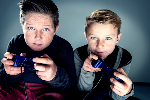 Close up portrait of two brothers, 8 and 10 years old, with intense stares getting competitive and  giving each other a hard time whilst playing a Playstation game.
