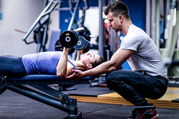 Personal trainer caring woman with her workout Personal trainer working with his client at a gym. Personal trainer caring woman. gym trainer stock pictures, royalty-free photos & images