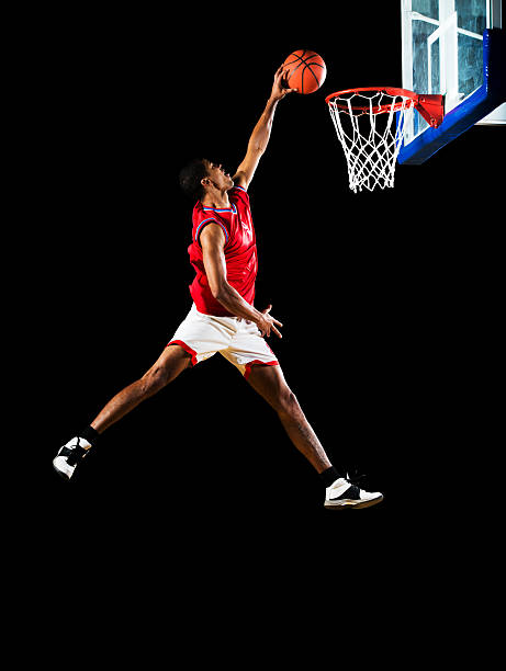 Slam dunking the ball. Young African American basketball player jumping high and slum dunking. Isolated on black. slam dunk stock pictures, royalty-free photos & images