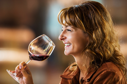 Side view of smiling mature woman enjoying while drinking red wine.