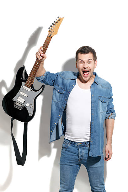 Portrait of young musician shouting with aggression. He is holding a guitar. Man is standing and looking at camera with anger