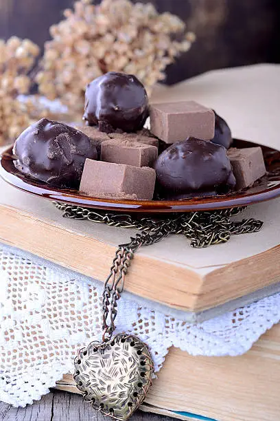 Chocolate truffles on old books with vintage lace on wooden table. Chocolate bonbon assortment closeup. Selective focus