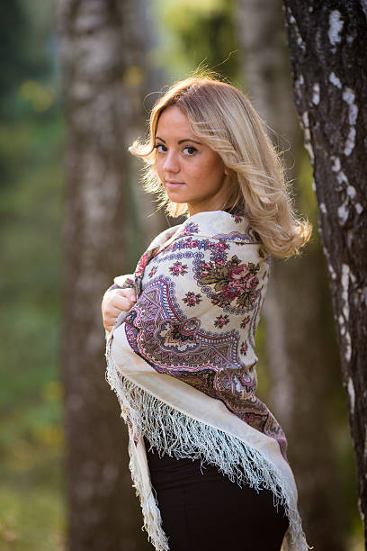 Young attractive woman at traditional shawl near the birch tree.