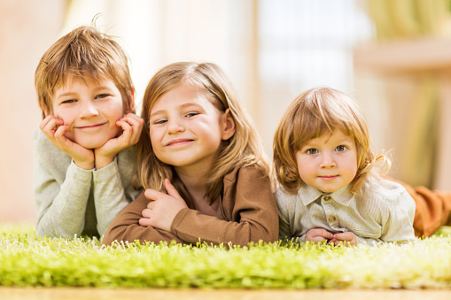 Smiling three children enjoying while lying down on carpet at home. They are looking at the camera.  