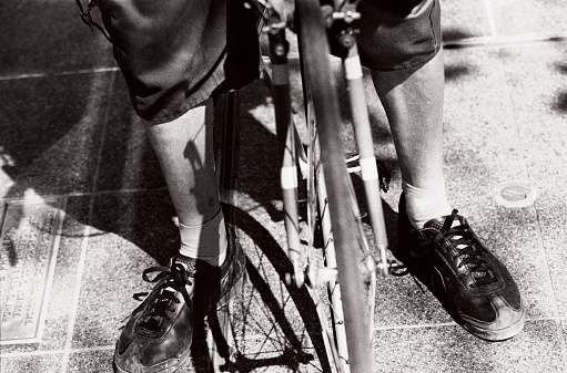 The legs and feet of a male bike messenger on the sidewalk next to a busy city street in San Francisco.