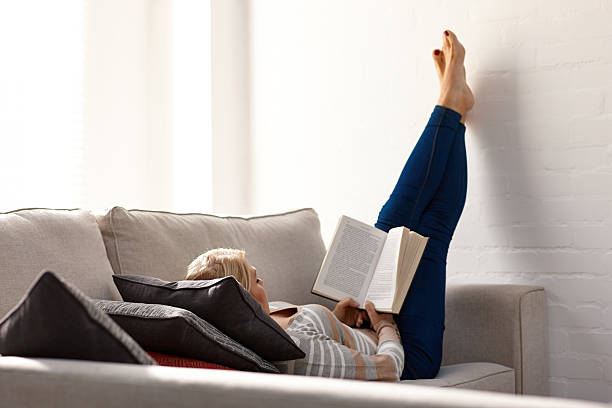 mulher madura relaxante no sofá a ler um romance - women book mature adult reading - fotografias e filmes do acervo