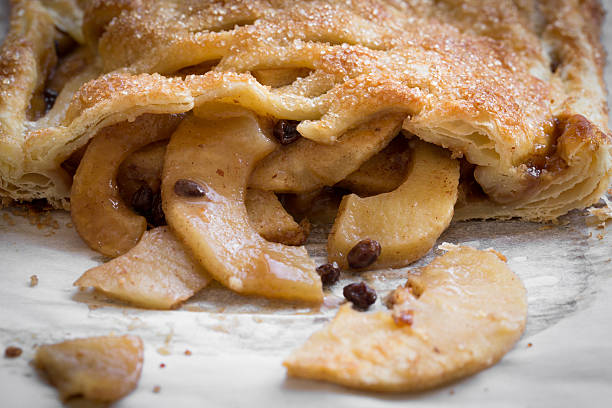 Apple Strudel A high angle extreme close up horizontal photograph of an apple strudel with some of the sliced apples and raisins spilling out of the pastry onto a parchment paper. apple strudel stock pictures, royalty-free photos & images