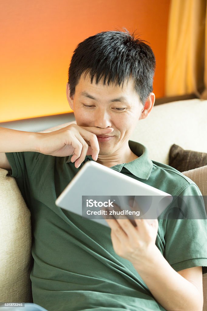 Asian young male adult looking tablet Asian young adult man using tablet and relax on sofa. Asian young male adult looking tablet Close To Stock Photo