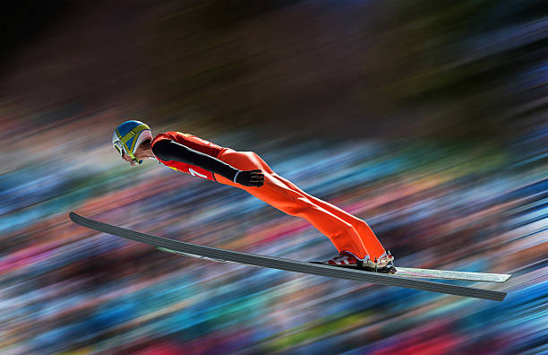 Ski jumper in mid-air against blurred background Side view of young male ski jumper during the long ski jump against the blurred background sportsman professional sport side view horizontal stock pictures, royalty-free photos & images