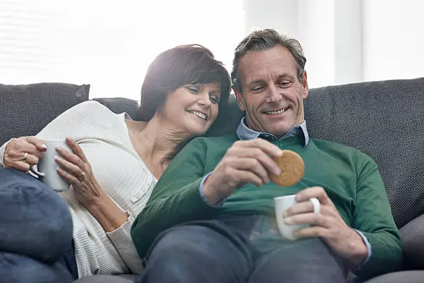 Photo of Beautiful mature couple relaxing on sofa with cup of coffee
