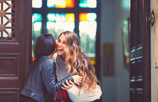 Young woman welcoming a friend to her home, embracing at the apartment building entrance