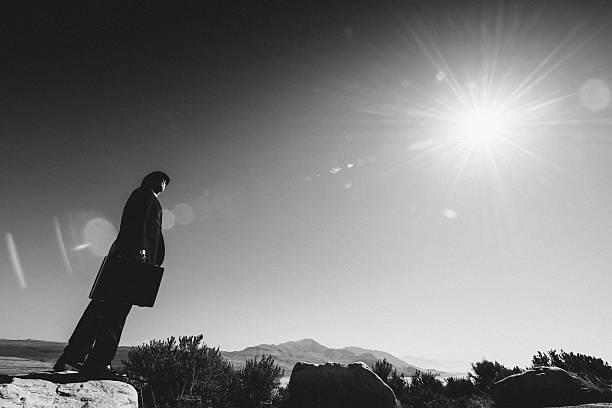 Old fashioned businessman carrying a suitcase and looking at the sun