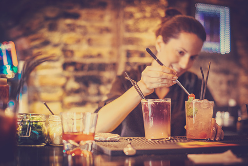 Portrait of bartender preparing a cocktails in a bar, she is putting cherry on top as a garnish