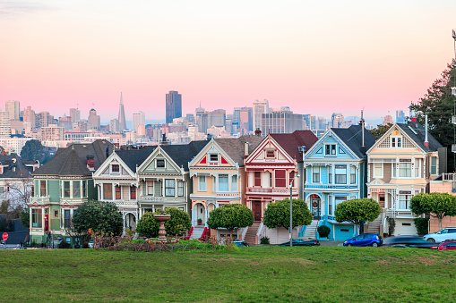 Classic shot of Victorian houses across the street from Alamo Square in San Francisco. Skyline of San Francisco is seen in background.