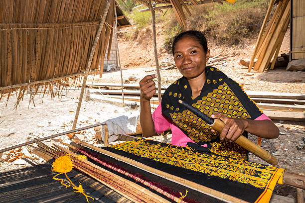 Asian woman traditionally weaving fabric Riung, Indonesia - September 30, 2014: A local Asian lady in Indonesia is traditionally hand weaving a batik or ikat in her village. ikat textiles at indonesian textile market stock pictures, royalty-free photos & images