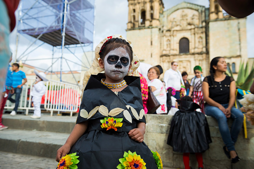 Oaxaca, Mexico - October 31, 2014: A Mexican girl stands in a crowd outside the Church of Santo Domingo de Guzmán in Oaxaca, Mexico. She and other children are dressed for Day of the Dead celebrations (