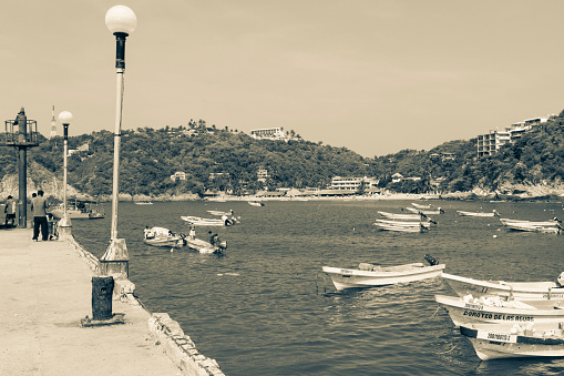 Puerto Angel, Mexico - August 3, 2014: Men fishing from the pier during the weekend, with fishermen boats docked at right, in this town by the sea in Oaxaca, Mexico