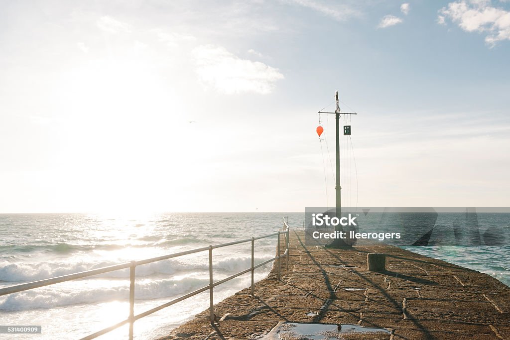 Porthleven pier and mast on the south coast of Cornwall Porthleven pier and warning mast at the harbours entrance in Cornwall, England. The stone pier extends out into the Atlantic a short distance where waves are breaking. It is later afternoon and the sun is nearly setting. Cornwall - England Stock Photo