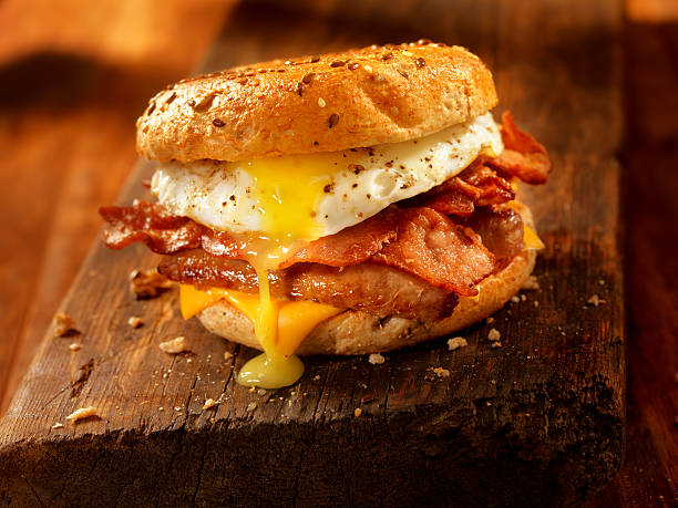 ベーグル、ベーコン、ソーセージ、エッグの朝食サンドイッチ - eggs sausage cheese meat ストックフォトと画像