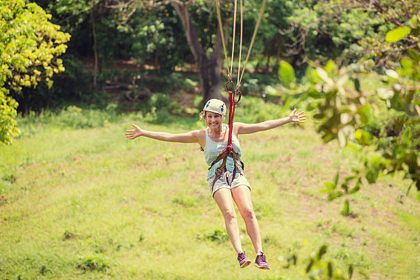 Happy woman riding a zip line in a lush tropical forest Happy smiling woman riding a zip line in a lush tropical forest while on family vacation. Arms spread wide showing her excitement canopy tour photos stock pictures, royalty-free photos & images