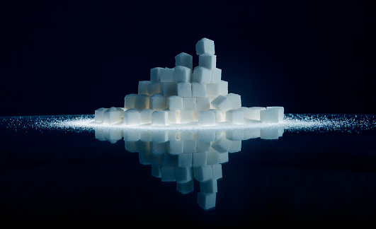 A reflected pile of stacked sugar cubes that looks like it's floating in space. Bands of sugar extend out to the edges of the frame. The image is toned and the background is dark with room for copy space (stock image).