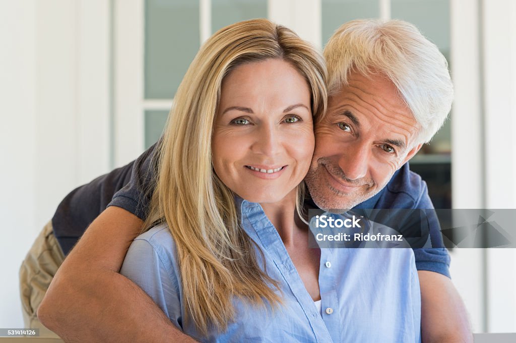 Man embracing woman Portrait of a senior smiling couple looking at camera. Senior man embracing behind his wife. Happy smiling retired couple in love. Couple - Relationship Stock Photo