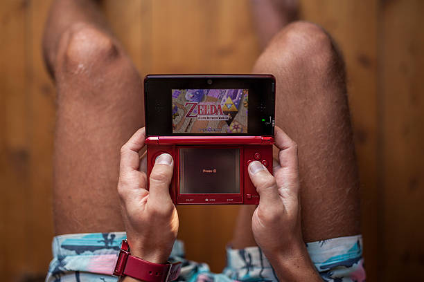 Gothenburg, Sweden - January 07, 2015: Gothenburg, Sweden - January 07, 2015: Zelda A Link Between Worlds is a game from 2013 developed by Nintendo Co., Ltd for their handheld gaming device Nintendo 3DS, also seen in the photo. The device is held by a young man in shorts.