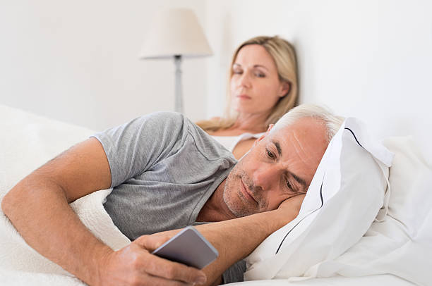 Cellphone abuse Jealous woman spying her husband mobile phone while he is reading a message. Senior couple in bed while wife is angry as husband using smartphone. Senior husband ignoring wife and texting on smartphone. double bed photos stock pictures, royalty-free photos & images