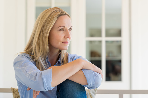 Woman sitting outside the house and thinking about her new idea. Pensive mid woman relaxing at home on a holiday. Portrait of mature woman planning her future.