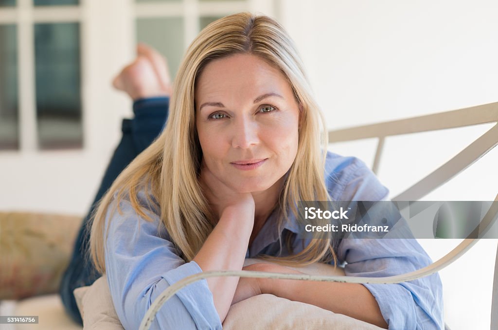 Woman relaxing Casual mature woman lying on front looking at camera. Happy mid woman lying on bench in the porch. Portrait of mature healthy woman relaxing at home. Mature Women Stock Photo