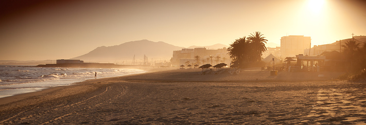 Colorful sunset in Marbella - Spain, beautiful empty beach, mountains and city in background.