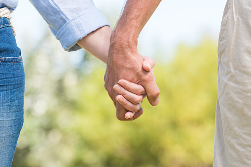 Closeup of couple holding hands outdoor. Romantic mature couple walking and holding hands. Close up hands of senior couple.