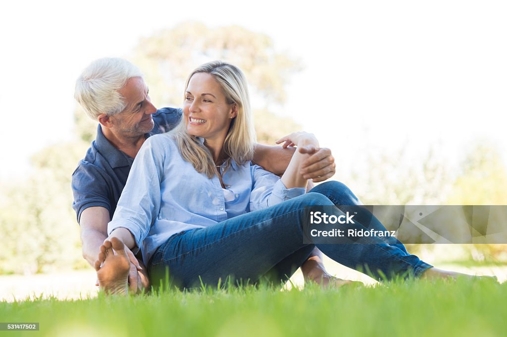 Senior couple in park Senior couple sitting in park. Happy smiling couple sitting on grass. Portrait of a senior man and woman relaxing at park and looking at each other. Mature Couple Stock Photo
