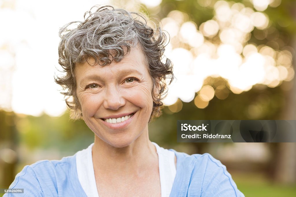 Smiling senior woman Portrait of senior woman relaxing at park. Close up face of happy senior woman looking at camera. Portrait of a smiling mature woman with grey hair. Mature Women Stock Photo