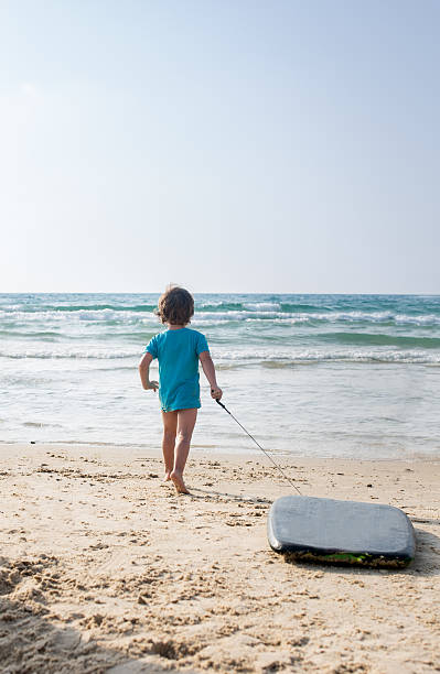 istock Back view of boy walking with surfboard on the beach. 531425778