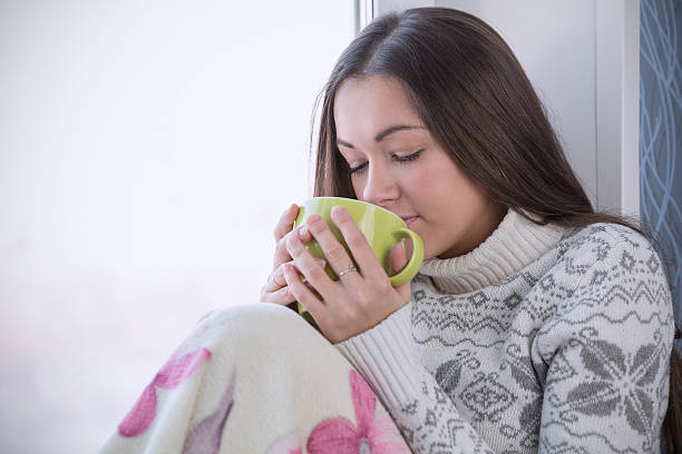 istock brunette in sweater and cup on window sill 531432351