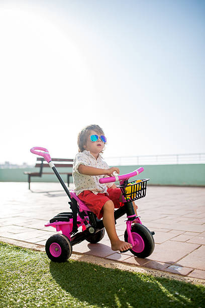 Funky little boy wearing sunglasses and sitting outdoors on his tricycle.