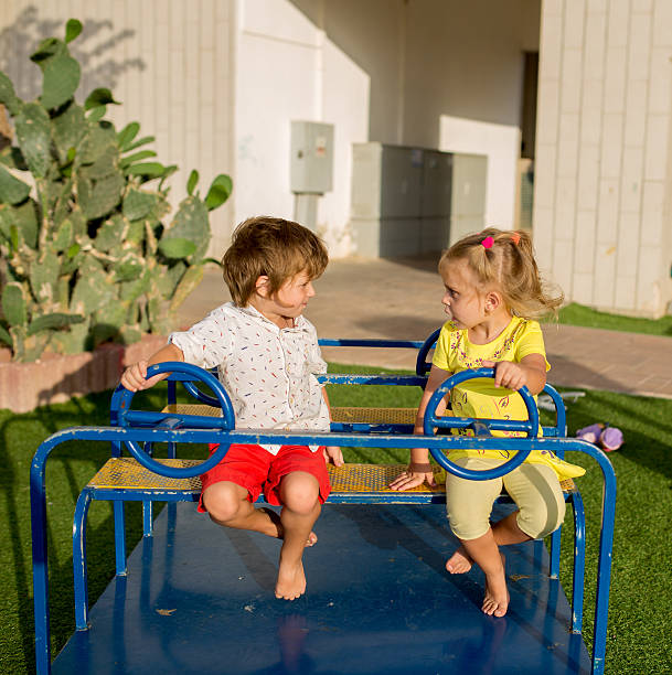 Boy and girl resting heads on elbows, looking at each other from blue playground.