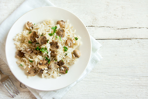Mushroom risotto with parsley on white wooden background with copy space