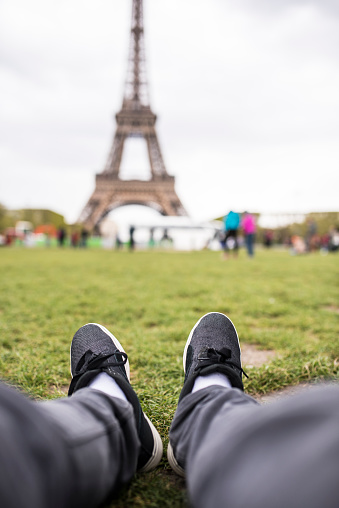 POV shot of a young adult sitting in the park looking at the Eiffel Tower