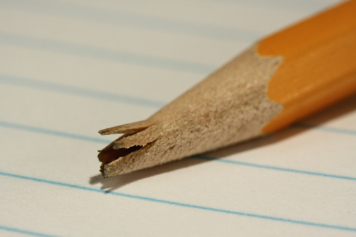 A close up pictureof the broken tip of a pencil with a shallow depth of field against lined note paper.