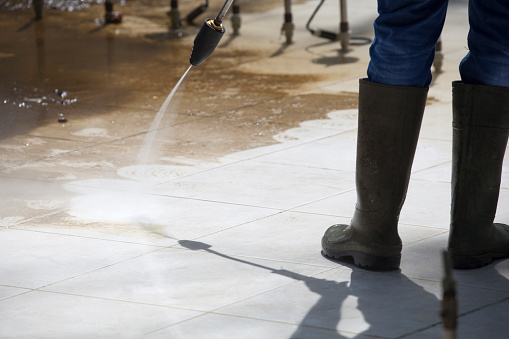 Worker in rubber boots, cleaning an outdoor fountain by pressure washer in a sunny day.