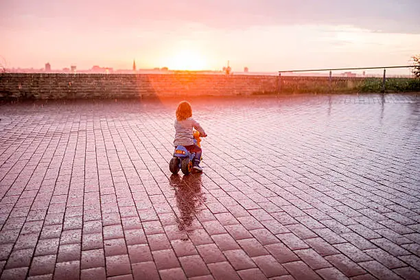 Photo of Back view of child driving toy motorcycle at sunset.