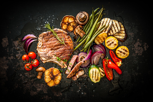 Beef T-Bone steak with grilled vegetables and seasoning on dark background